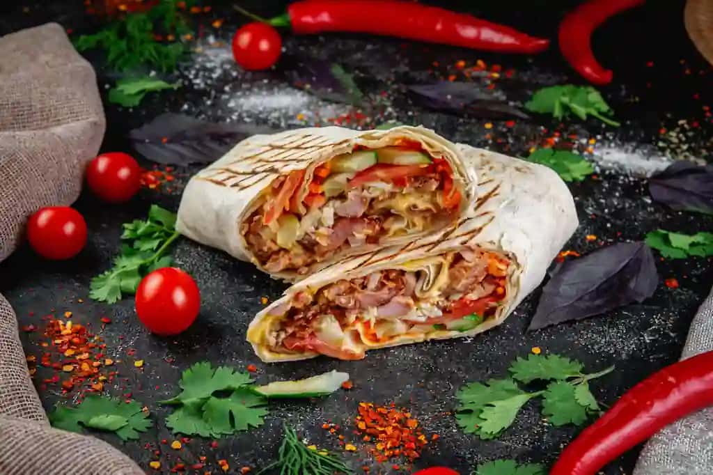 Sabzavotli o'tlar bilan kesilgan Shawarma burrito qorong'u tosh stol tushunchasi tez ovqatlanish restoranlari | Shawarma burrito cut with vegetables herbs dark stone table concept fast food restaurants