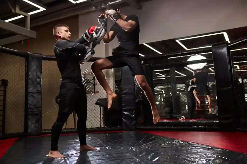 Professional mma jangchisi o'zini himoya qilish usullarini o'rgatadi va yosh bokschi turli xil texnikalarni birgalikda mashq qilishini ko'rsatmoqda. | Professional mma fighter teaches self defense tricks showing it young boxer practice different techniques together sport workout concept side view copy space