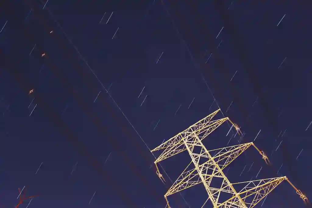 Osmonga qarama-qarshi bo'lgan past burchakli ko'rinishdagi elektr ustuni, kechasi yulduzli yo'llar | Low angle view electricity pylon against sky with star trails night