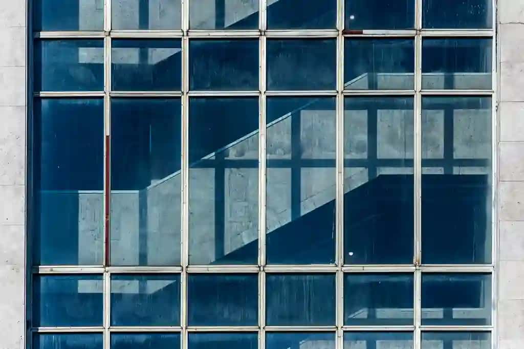 Yuqori texnologiyali ofis binosi shaffof devorlari yorqin ko'k osmonni aks ettiruvchi bulutlar bilan zamonaviy arxitektura mavhum shisha fon | High tech office building with transparent walls reflecting bright blue sky with clouds modern architecture abstract glass background