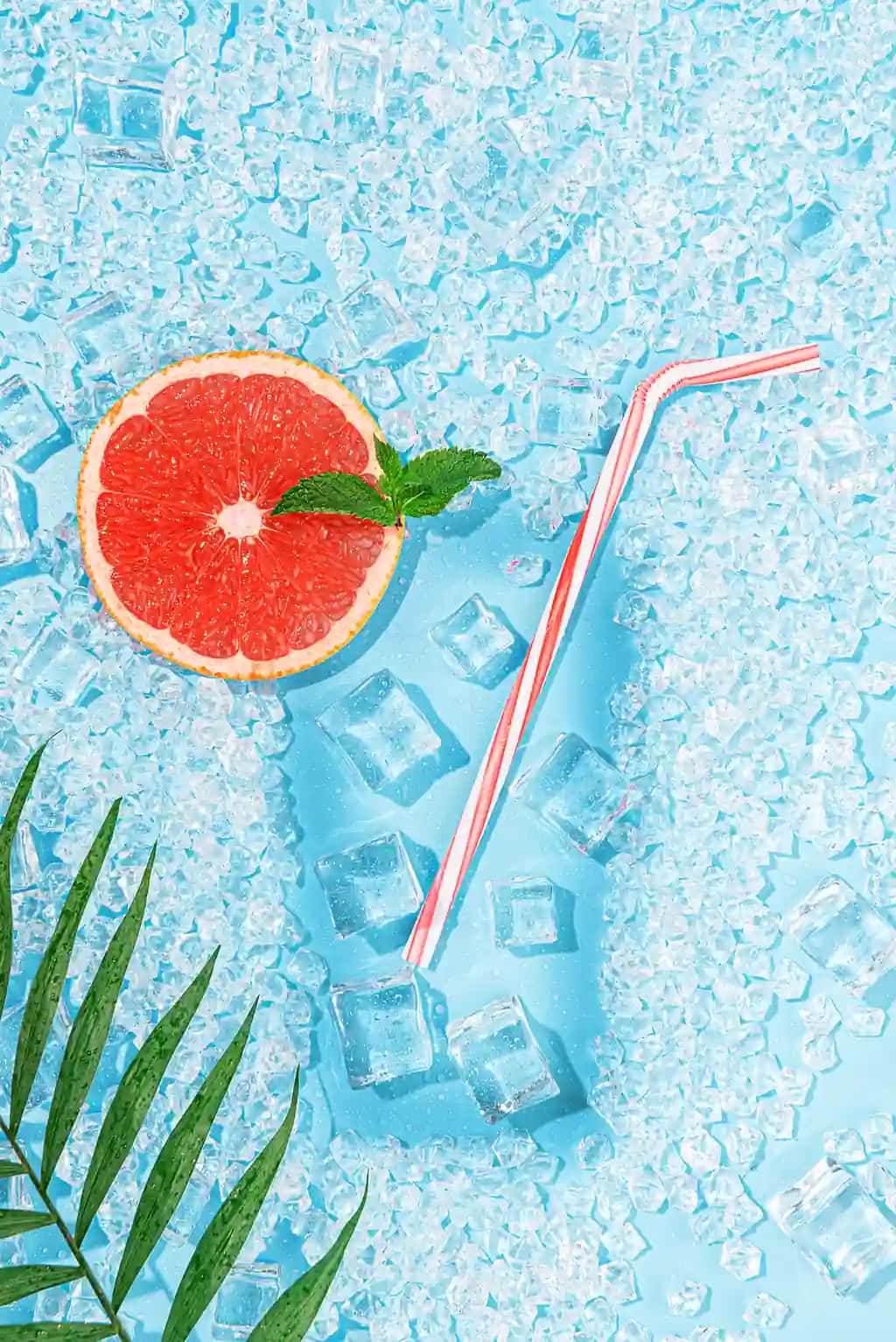 Ochiq ko‘k fonda muzli sovuq ichimlik, shisha kokteyl bo‘lagi bilan greyfurt | Cold drink ice light blue background laid out form glass with tubule cocktail slice grapefruit