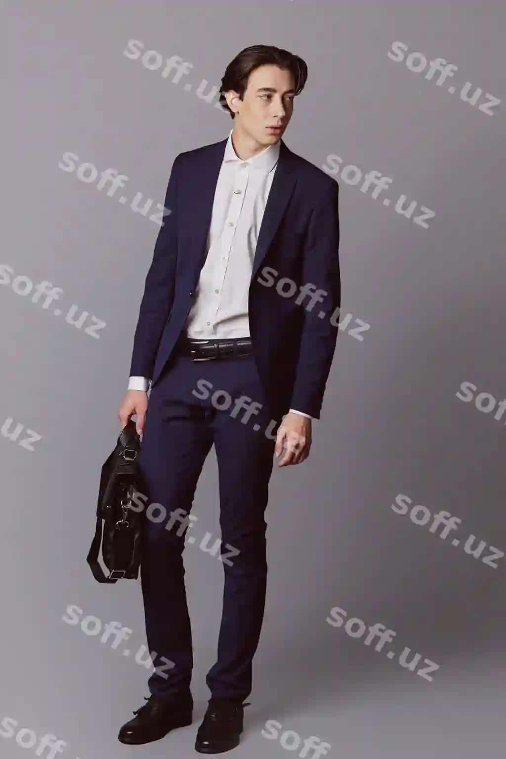 Yosh erkak ko'k rangli kostyum qora biznes sumkasi bilan kulrang devor. | Young man navy suit with black business bag gray wall