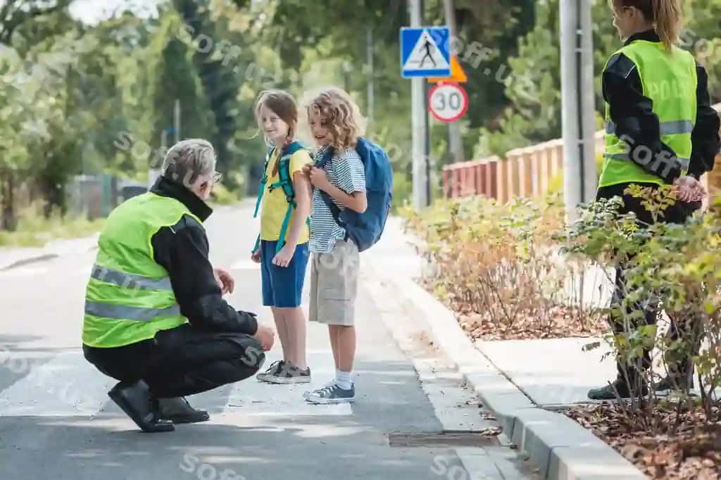 Oldinda cho'kkalab o'tirgan politsiyachi guruh maktab o'quvchilariga qanday qilib kesib o'tishini tushuntirmoqda | Policeman crouching front pedestrian explains group school children how cross