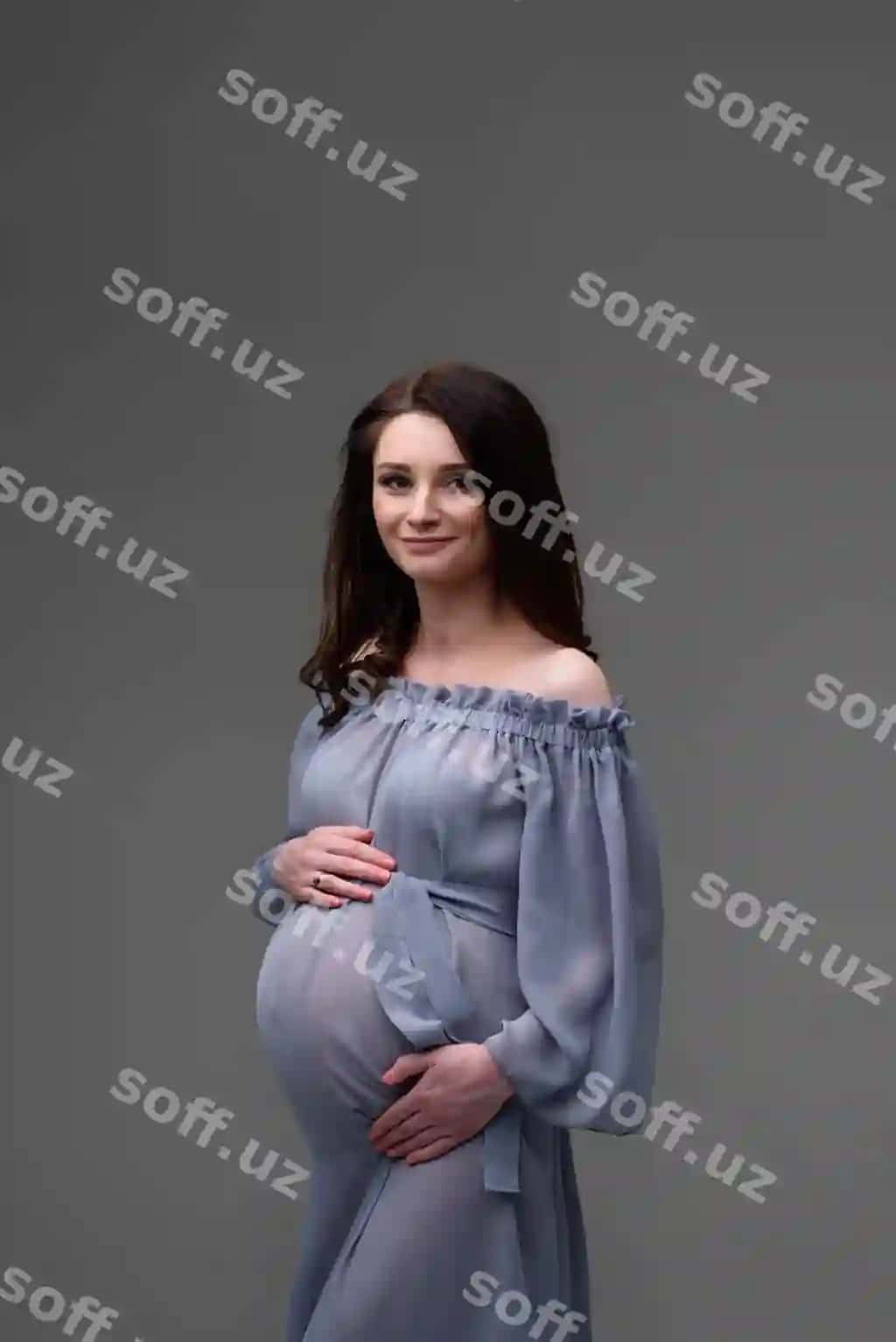 Yosh homilador ayol kiyimi kulrang devor yonida turibdi. | Young pregnant woman dress stands gray wall